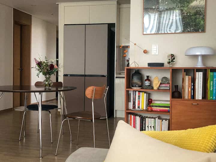 Natural brown wood tone dining room featuring round dining table, wooden chairs, bookshelf with various objets in cozy setting