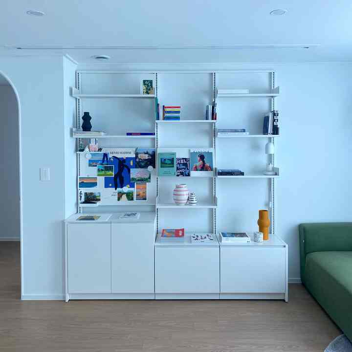 White and natural color study space featuring a modular system shelf and green sofa with clean, modern decor