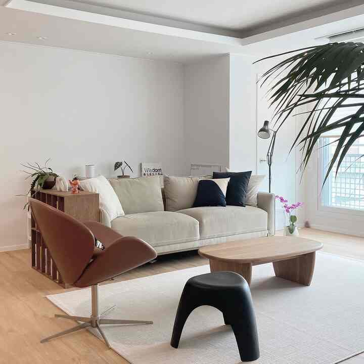 Bright white living room with wood tone floor, natural wood coffee table, beige sofa, and brown armchair in a modern setting