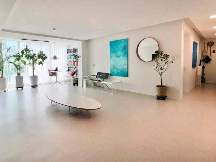 A spacious and open living room with white and natural color tones, featuring plants, a round mirror, and an elliptical table in a minimal modern style
