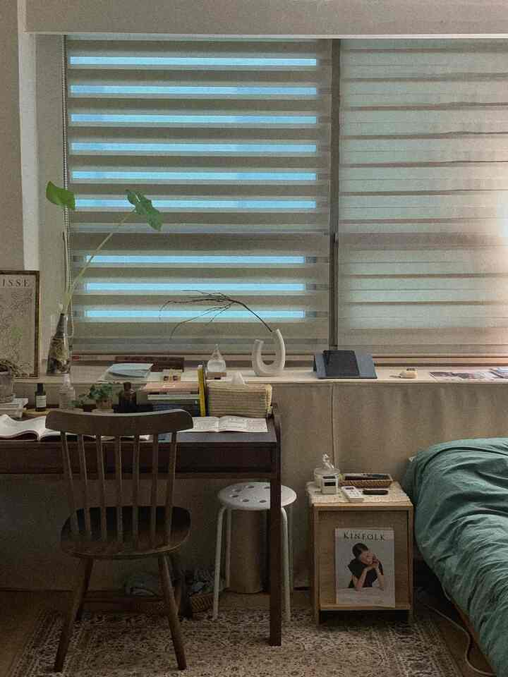木目調とナチュラルカラーの寝室兼書斎空間、窓にカーテンと机、椅子が配置された雰囲気のあるインテリア