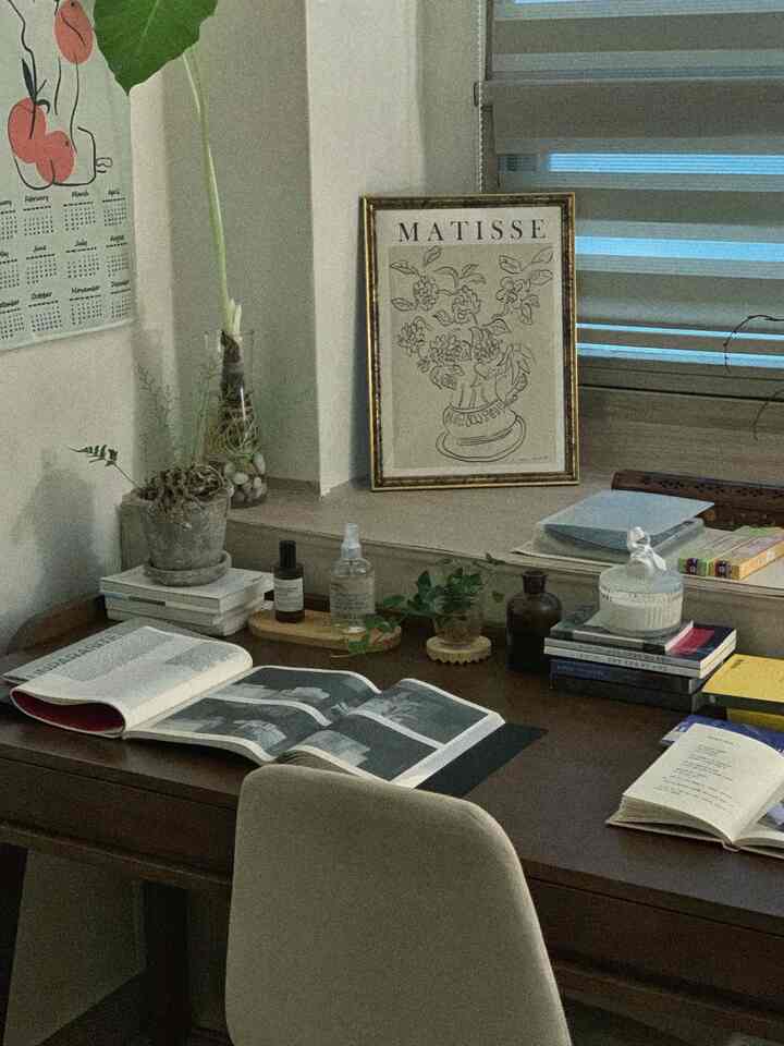 Natural brown-toned study space featuring wooden desk and chair, plants, and framed artwork creating a quiet reading and workspace
