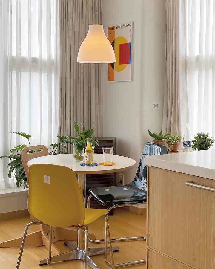 白とライトブラウンの色調のダイニングルーム、黄色と黒の椅子と植物が配置されたモダンでシンプルなインテリア