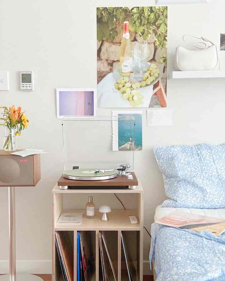 柔らかなナチュラルカラーと青の花柄寝具が配置された、ターンテーブルと小さなテーブルランプのある居心地の良い寝室