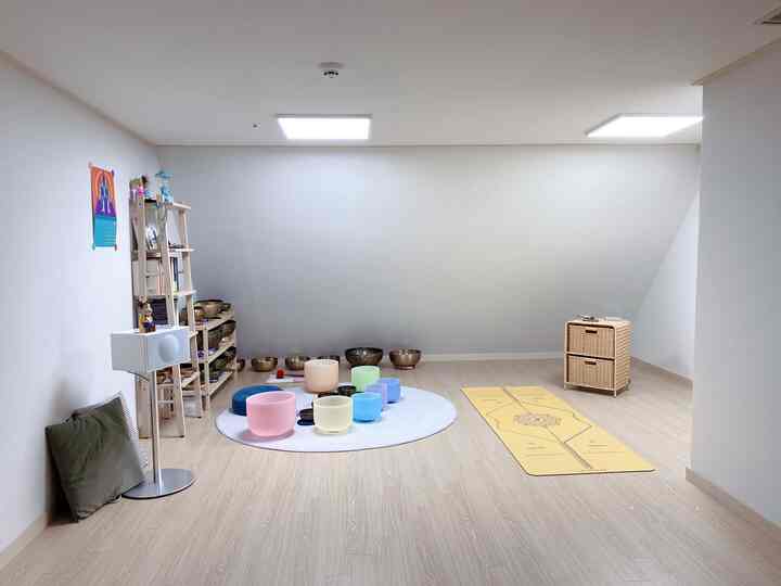 Bright natural-toned yoga room featuring colorful meditation sound bowls and a yellow yoga mat in a serene workspace
