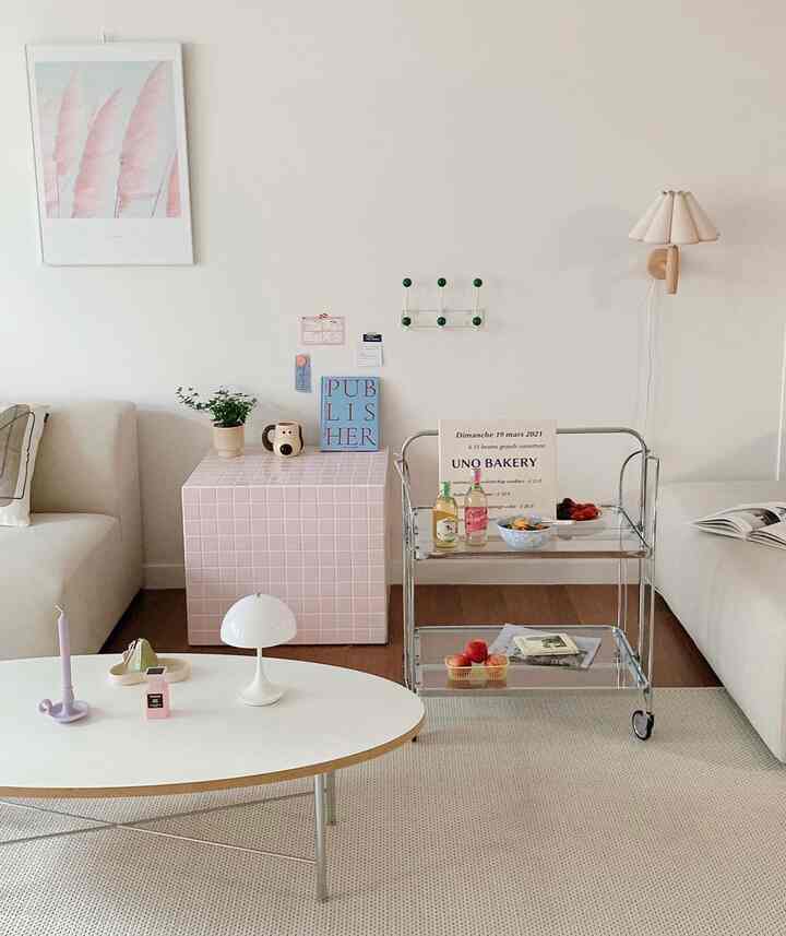 白を基調としたリビング、ピンクのタイルサイドテーブルとヴィンテージのガラストロリーが配置された雰囲気のあるモダンな空間