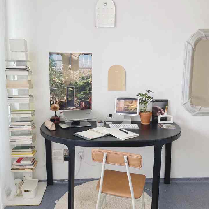 A compact home office with white walls and dark gray furnishings, featuring a black desk and leather chair in a simple, clean atmosphere