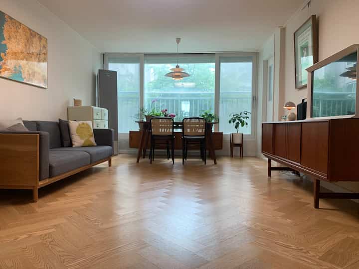 Natural wood tones and herringbone flooring in a living-dining room featuring a gray sofa and wooden sideboard with a modern, cozy atmosphere