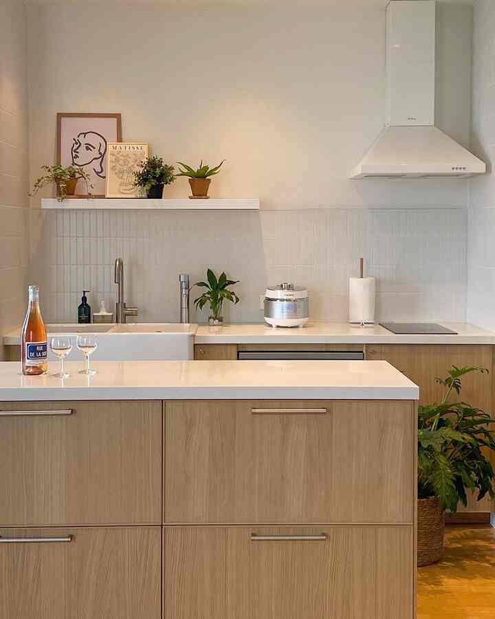 White and wood tone kitchen space featuring plants and wine glasses, creating a cozy home restaurant atmosphere