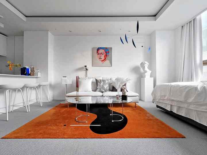 A white and orange tone living room featuring a glass coffee table, sofa, modern art on wall, and a hanging mobile creating a clean space