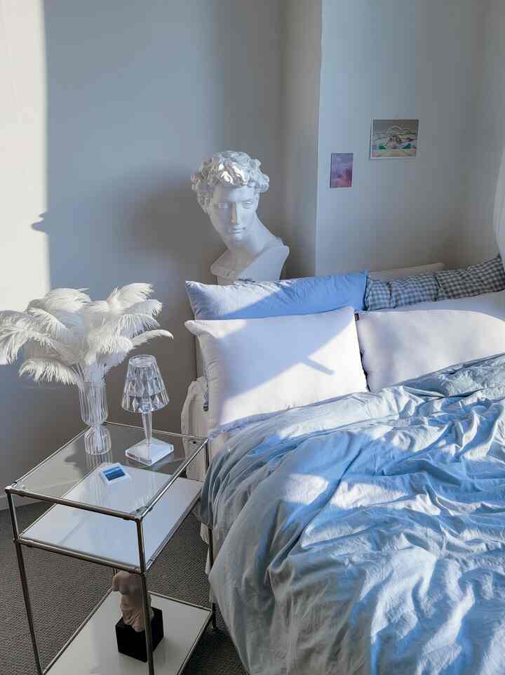 Bright bedroom with white walls and blue bedding, featuring a side table and classical bust sculpture for a calm atmosphere