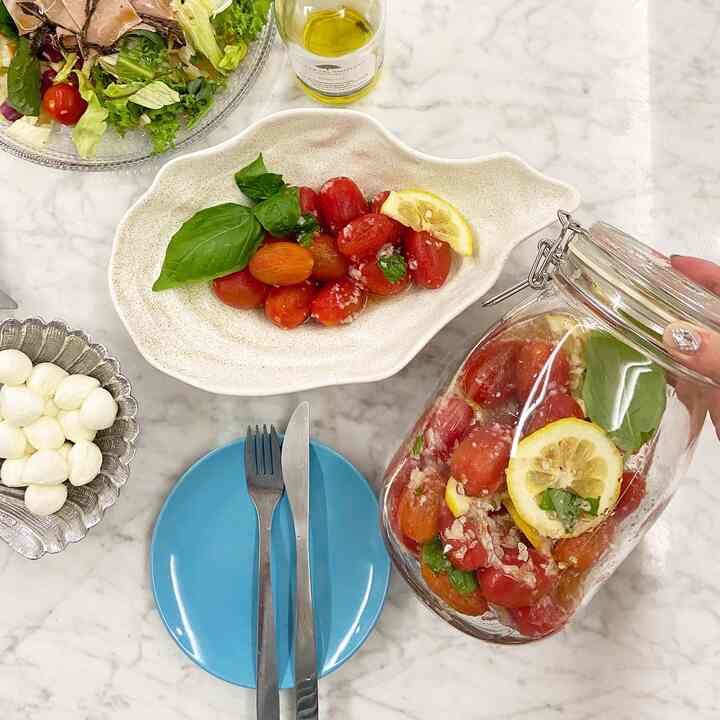 白い大理石のテーブルに透明な瓶と陶器のボウルが配置され、赤いチェリートマトとバジルが彩る爽やかなキッチン空間