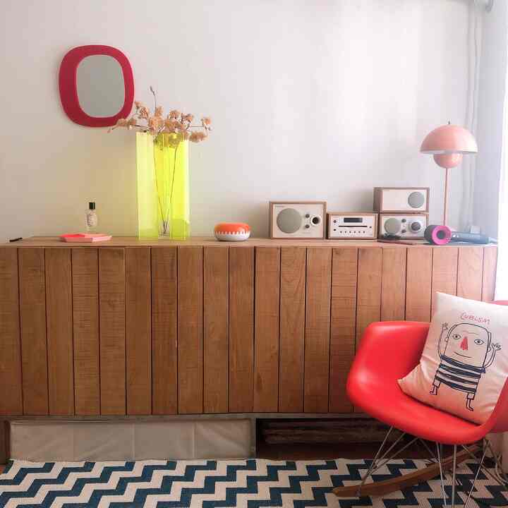 Retro mood bedroom in orange and pink tones featuring an Eames armchair and Tivoli audio set on a wood tone console