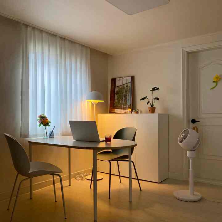 ホワイトとナチュラルトーンの2人用ホームオフィス兼ダイニング、シンプルな家具とフロアランプが配置された落ち着いた空間