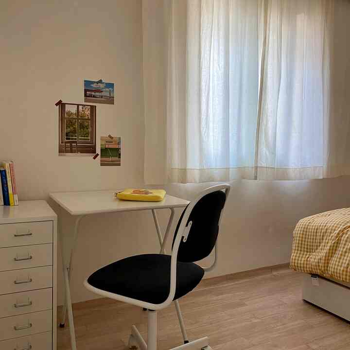 White and natural color toned single-occupancy bedroom featuring a simple desk, office chair, and cozy bed with yellow checkered bedding
