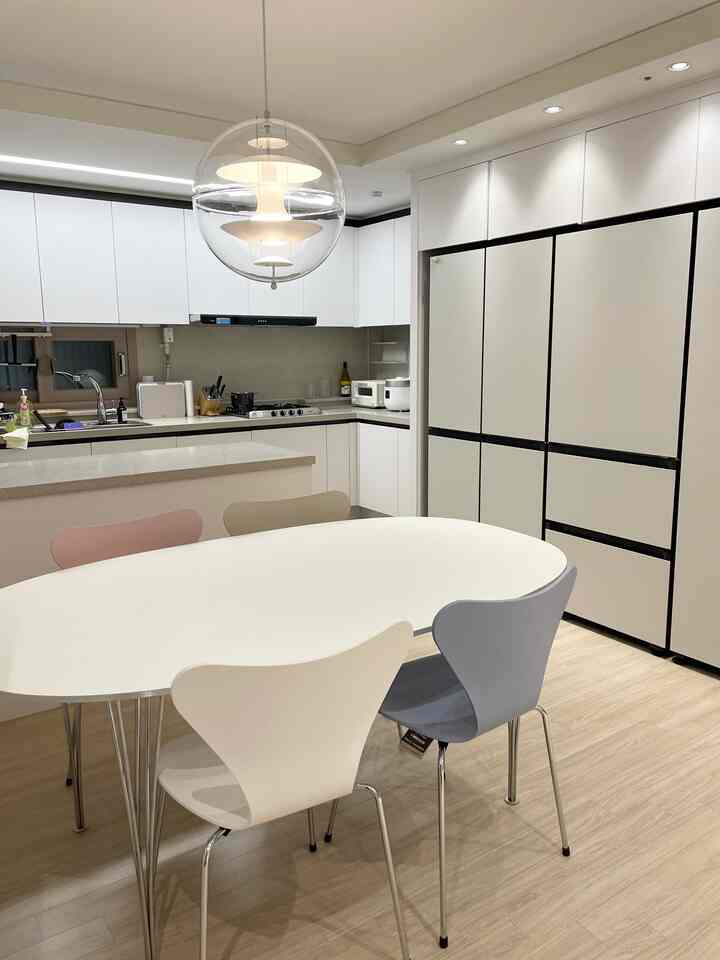 White and natural tone kitchen and dining room featuring a white dining table and multicolored dining chairs in a clean modern space
