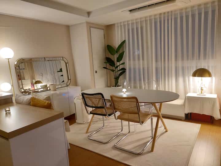 ホワイトとゴールド調のワンルームダイニング兼おうちカフェ空間、明るい照明と植物で居心地の良い雰囲気