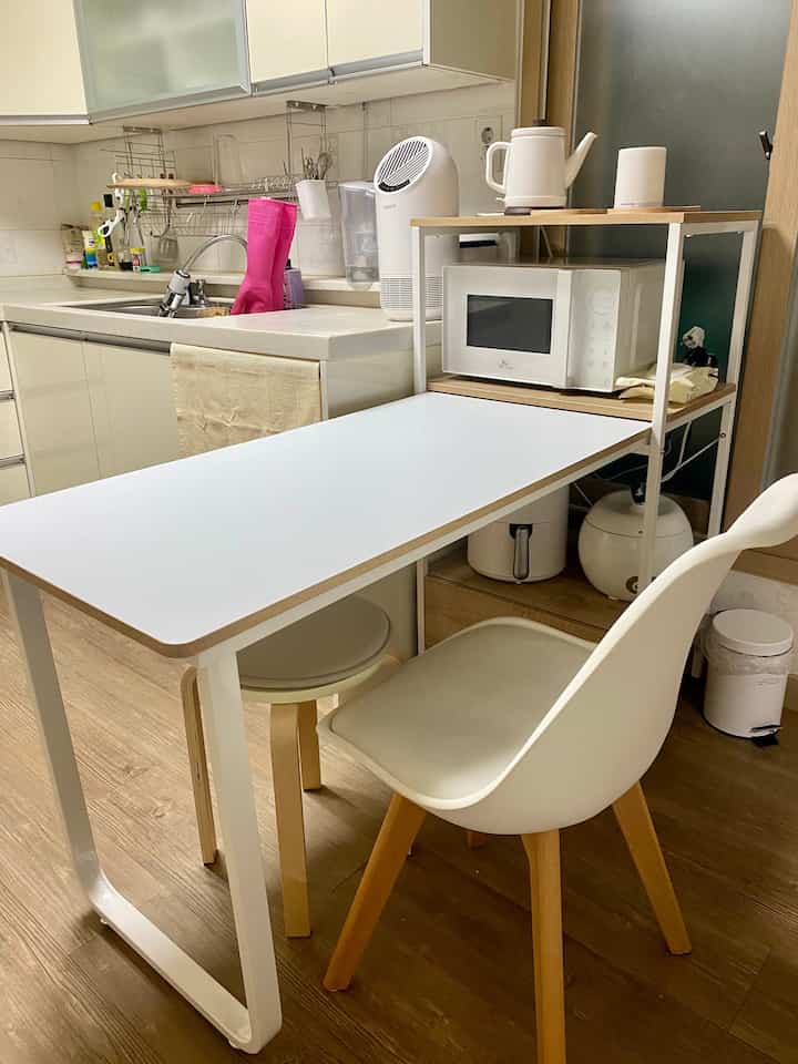 White and wood tone compact kitchen and dining area featuring microwave and air fryer, practical space suitable for a single household