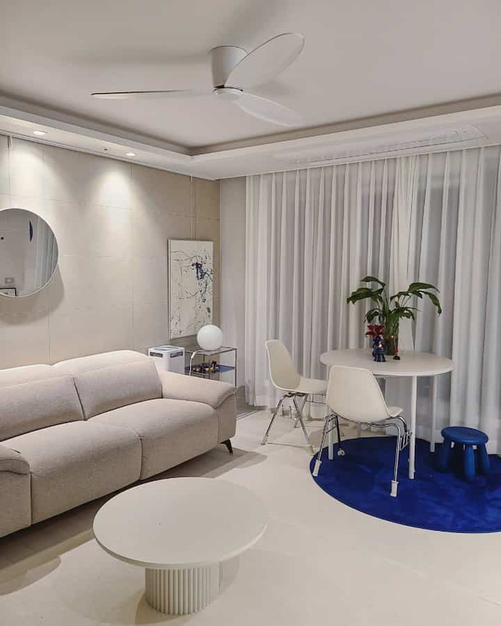 White-toned living room featuring mid-century modern sofa, round tables, and a blue round rug creating a harmonious modern interior