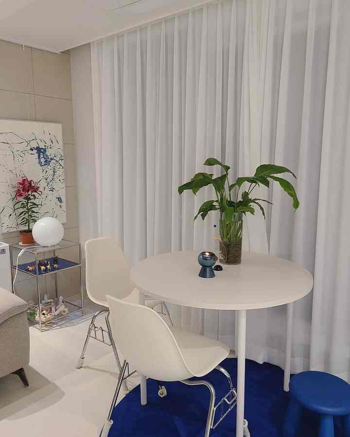 ホワイトとブルーの色調のリビング兼ダイニングスペース、円形の白いダイニングテーブルと椅子、青いラグと植物の装飾が配置された清潔感あるインテリア