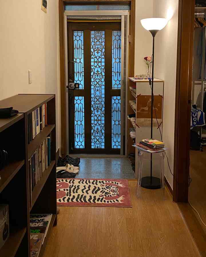 Cozy small entrance featuring natural wood tones, white walls, a bookshelf, shoe cabinet, and floor lamp providing a warm atmosphere