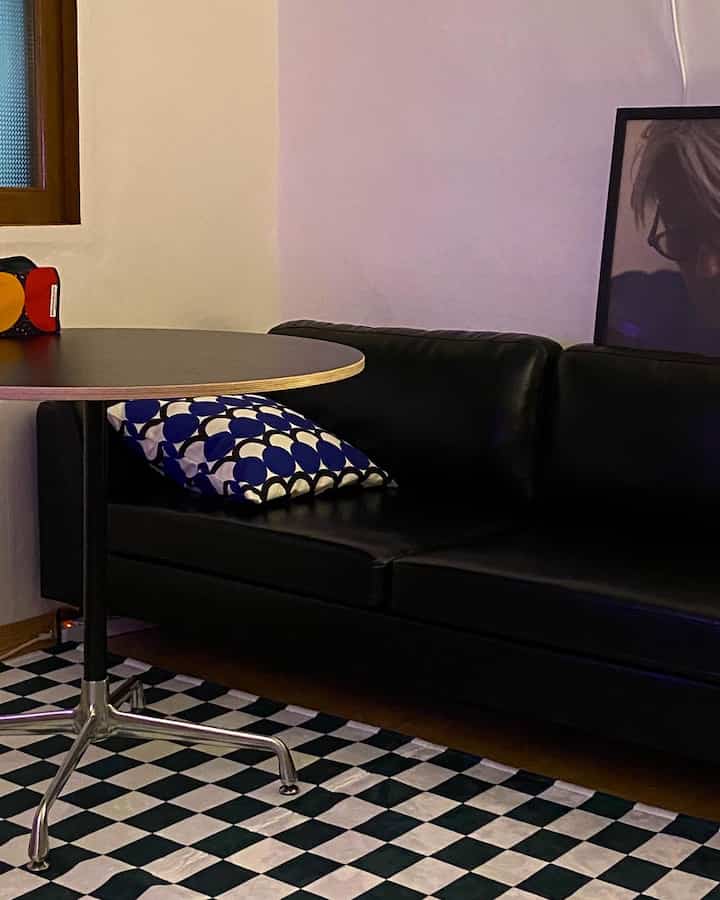 Black and white toned living room featuring a round table, leather sofa, and checkerboard rug creating a modern cafe-style atmosphere