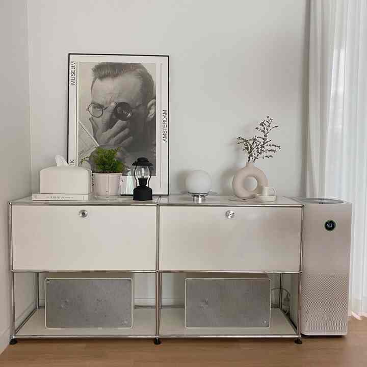 ホワイトトーンのキッチンの一角、モダンな収納キャビネットに額縁と多様なインテリア小物が配置された清潔感のある空間