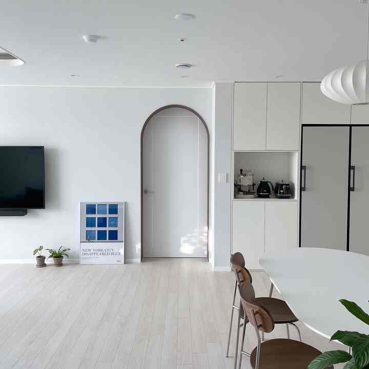 Modern living room and kitchen space with white and wood tones, featuring an art poster and dining table setup
