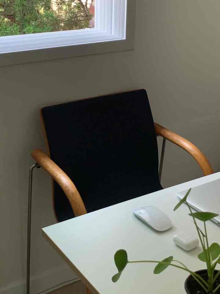 A calm home office space featuring a white desk and natural wood-toned armchair with minimal accessories on the tidy desk surface