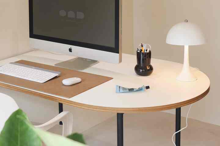 White-toned home office space featuring a white desk, computer, and desk lamp with a sleek atmosphere