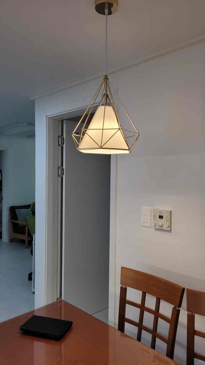 A gold and white toned kitchen space featuring a modern gold-frame pendant light and wooden dining table, creating a cozy atmosphere