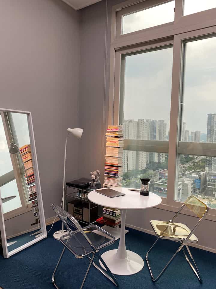 Modern living room with blue carpet and white furniture, featuring a home cafe setup near large windows with abundant natural light