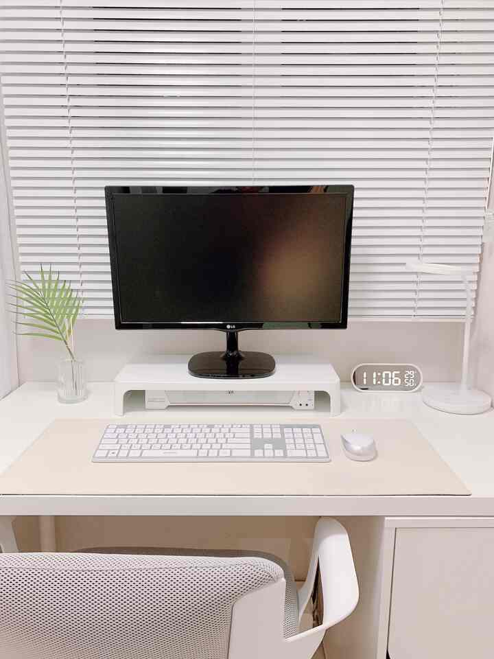 White-toned home office space featuring a clean desk with computer monitor and keyboard centrally placed, minimalist interior
