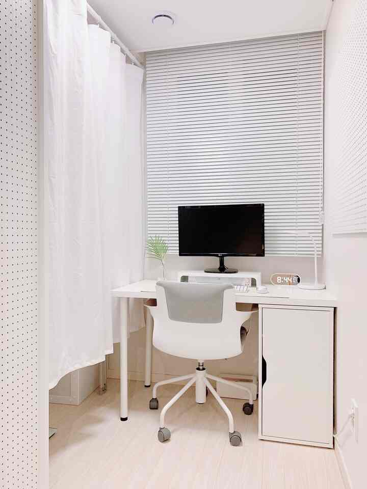 White-toned home office space featuring a centrally placed desk, chair, and monitor with a clean atmosphere