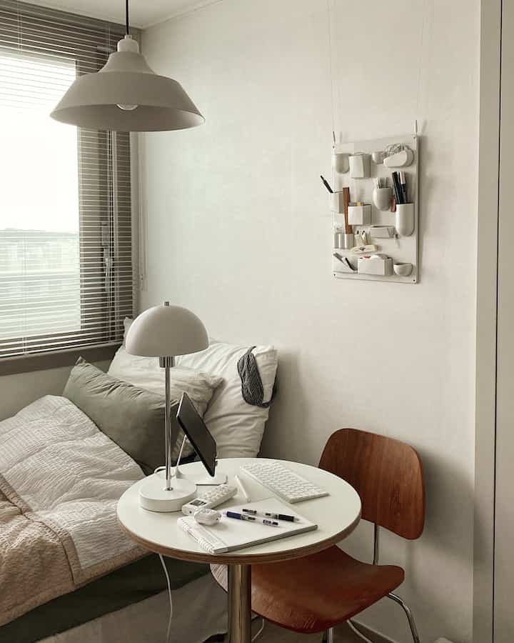 ホワイトとブラウンのナチュラルでシンプルな一人暮らしのホームオフィス、ベッドとデスク、テーブルランプが配置された落ち着いた雰囲気の空間