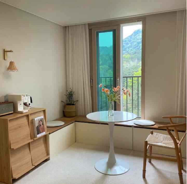 白と木目調のナチュラルなリビング兼おうちカフェ空間、窓際のベンチと丸テーブルが配置された雰囲気のあるインテリア