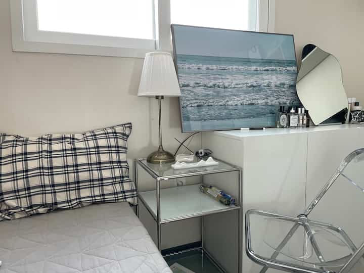 A small studio bedroom in white and gray tones featuring a bed, modular storage cabinet, and transparent chair with a modern vibe