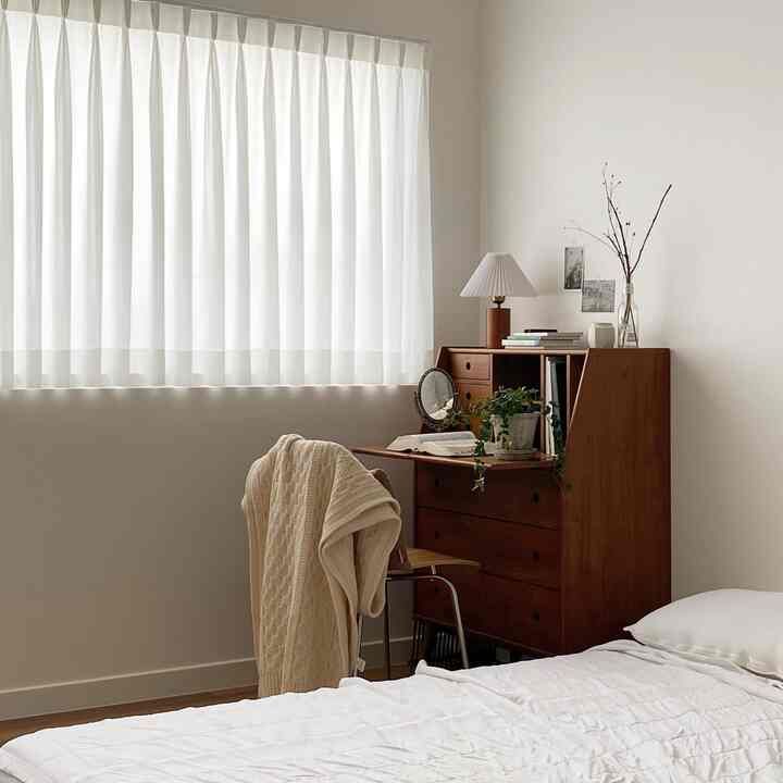 Natural modern bedroom with white walls and curtains, wood-toned desk and bed creating a calm atmosphere