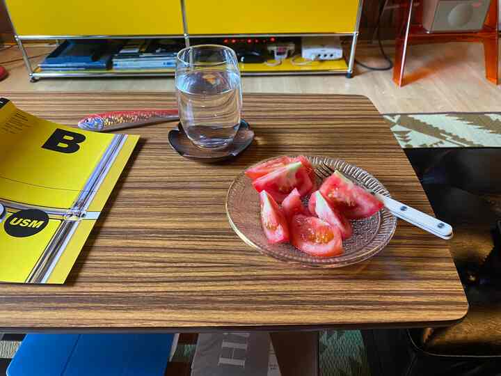 黄色の棚と木目調のテーブルが配置されたリビング、シンプルな果物と水のグラスがある落ち着いた雰囲気の空間