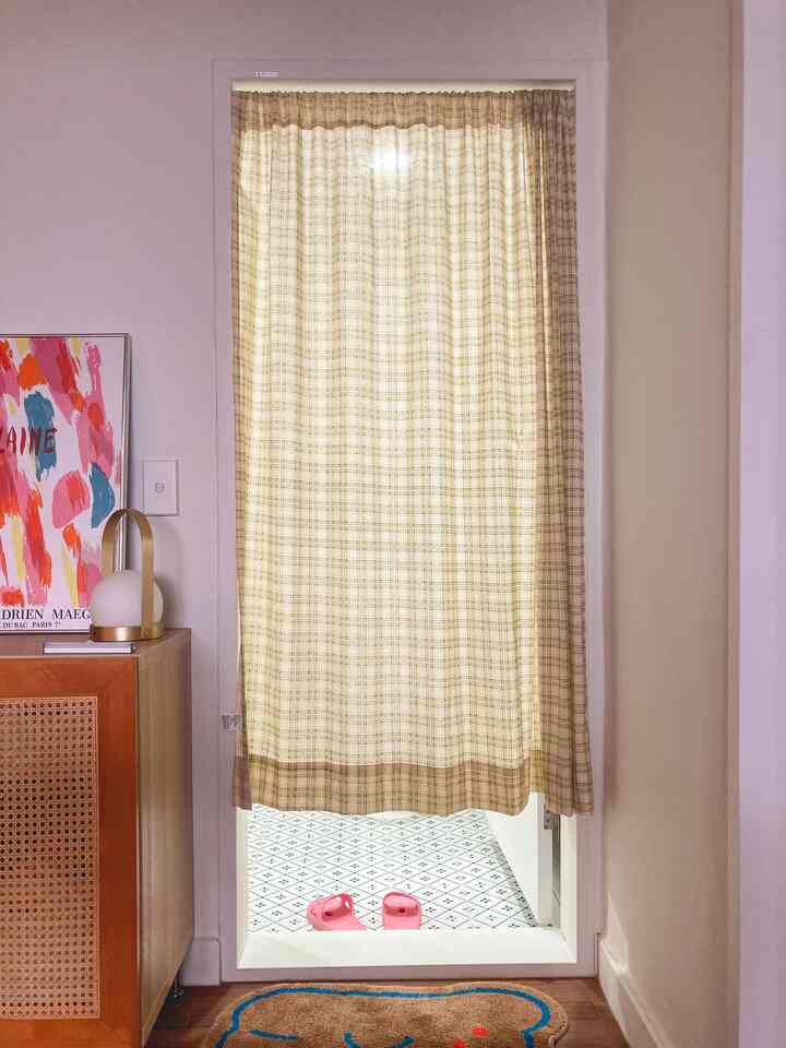 Beige-toned curtain covering bathroom entrance, cozy space with brown bath mat and colorful art poster