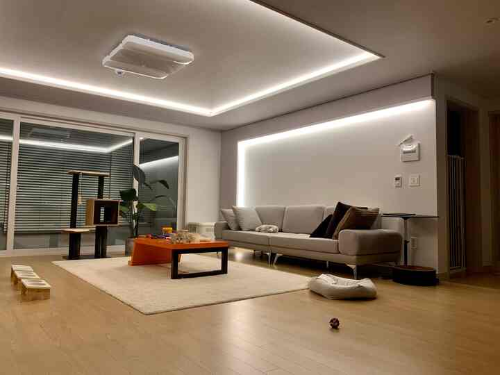 Modern living room with wood tone flooring, light gray sofa, orange coffee table and cat tower in a neat layout