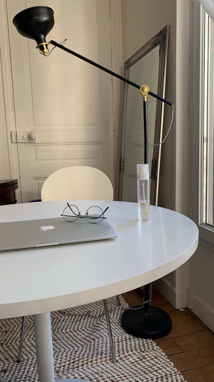 White-toned living room featuring a round white table and chair, vintage mirror, and black floor lamp in a simple vintage style space