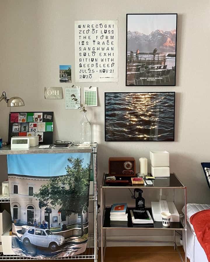 白い壁にさまざまなポスターが飾られた木目調の床の寝室、レトロなラジオが置かれたシンプルで居心地の良いホームオフィス環境