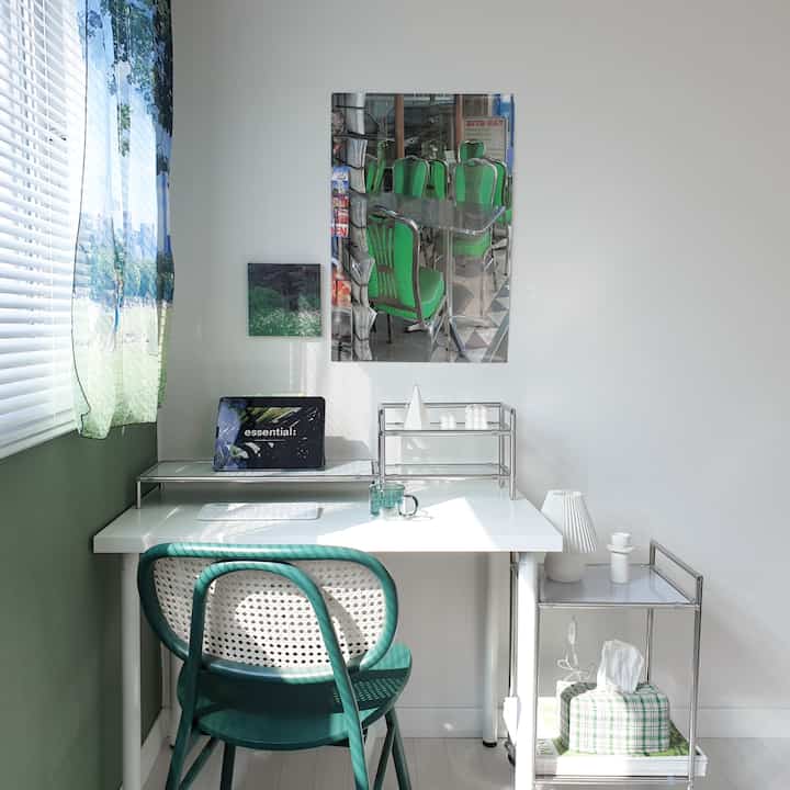 A bright home office space in white and green tones featuring a modern desk and chair arranged neatly in a minimal setting