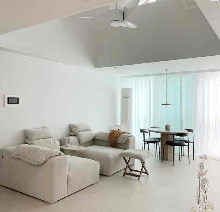 Bright white and beige-toned living room featuring wooden dining chairs and a marble dining table in a simple, high-ceiling open space