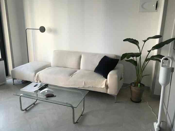 White-toned living room featuring a white sectional sofa and glass coffee table at center, with a simple atmosphere