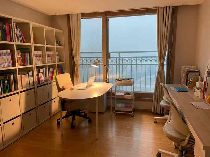 ベージュとウッドトーンのホームオフィス兼子供と暮らす空間、大きな本棚と机が配置された整理されたインテリア