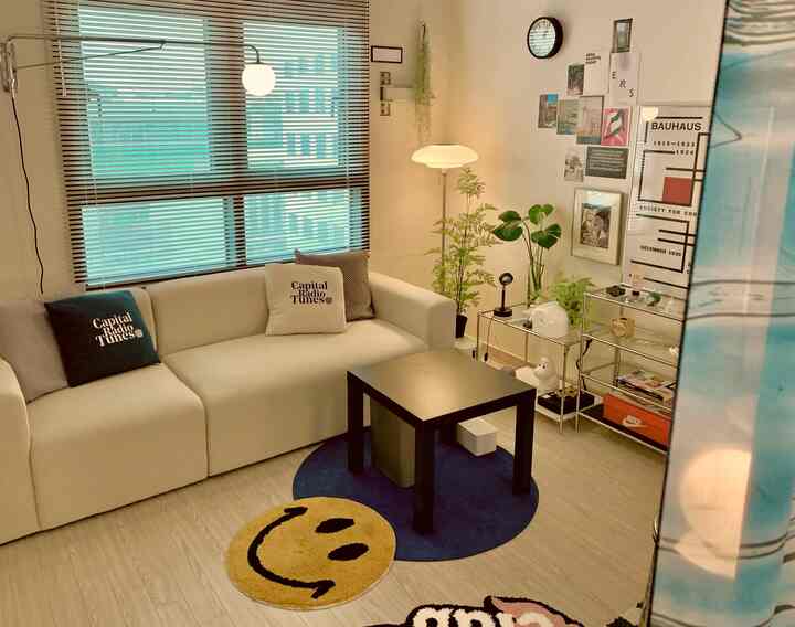Natural-toned studio living room featuring a white sofa, black coffee table, green plants, and artistic posters with a cozy ambiance