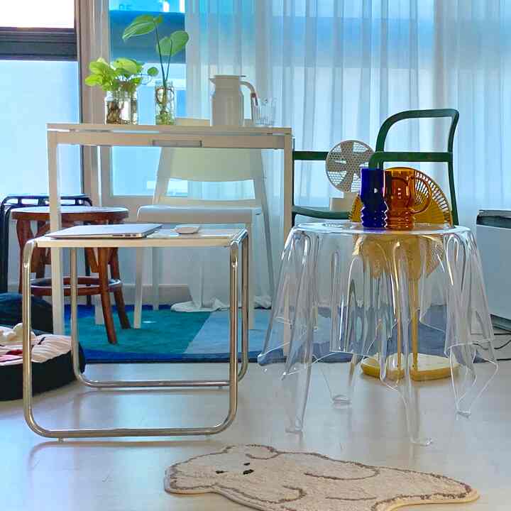 A studio living room dominated by white and transparent materials featuring an acrylic table, Mid-Century Modern chairs, desk, and stools in a cozy setting
