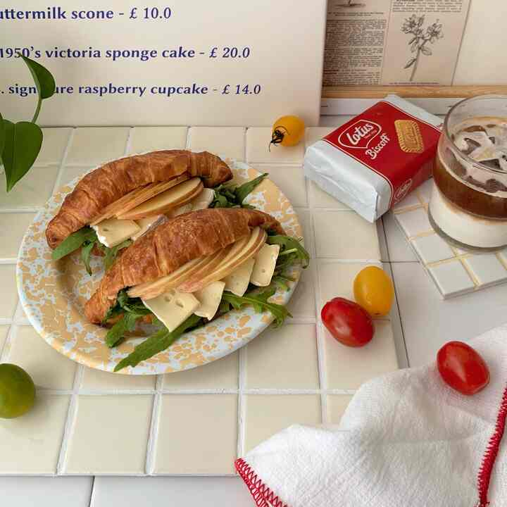 白とベージュの色調のキッチンスペース、タイルのテーブルにクロワッサンサンドイッチ、アイスコーヒー、クッキーが配置された雰囲気のあるおうちカフェ